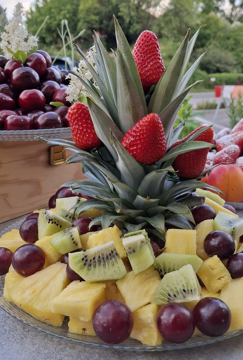 Vassoio di ananas a cubetti, kiwi e uva rossa con il ciuffo decorato da fragole, ciliegie in cassetta di legno dietro